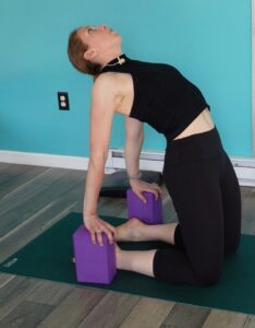 Dr. Chloe demonstrating the easiest version of camel pose for yoga for runners.  She uses blocks to help support her as she leans into her backbend